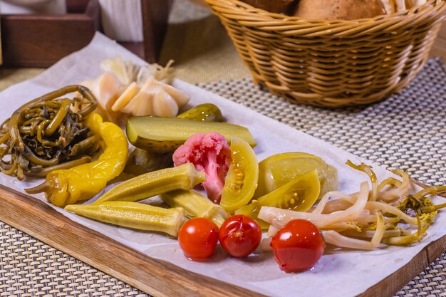 Foto diversi tipi di verdure sott'aceto su un piatto bianco. cetrioli sottaceto, pomodorini, verdure, funghi e aglio con cipolla e lattuga sul tavolo.