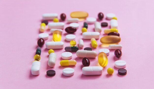 Different types of pills lie on a pink surface, medicine treatment, vitamins, antibiotic