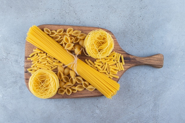 Different types of raw dry pasta on a stone surface.