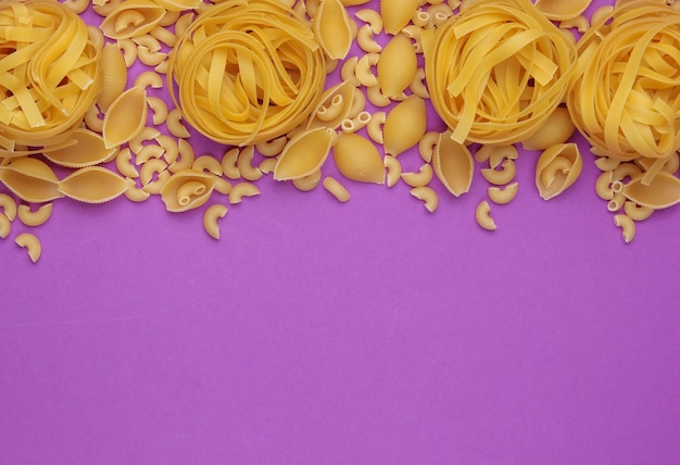 Foto diversi tipi di pasta italiana cruda su sfondo viola. vista dall'alto. copia spazio