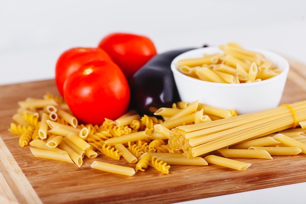 Different types of raw italian pasta with tomatoes and other vegetables top view background selected