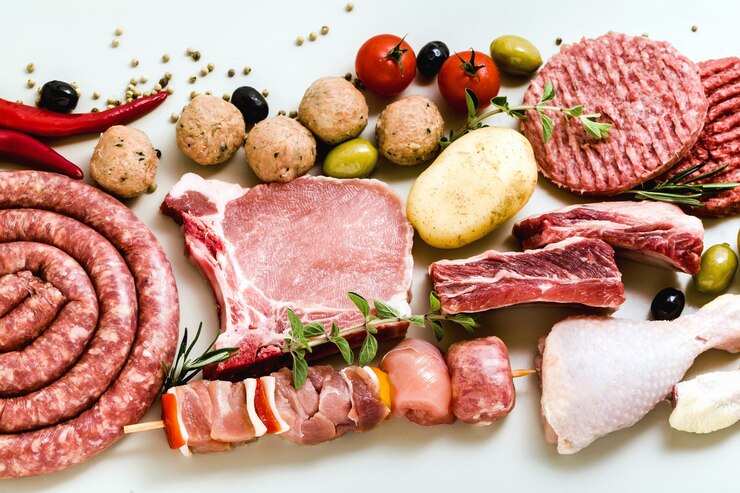 Different types of raw meat: chicken thighs, pork and beef burgers, ribs and kebabs, turkey meatballs, ready to be cooked with potatoes, hot pepper, olives and black olives and aromatic herbs