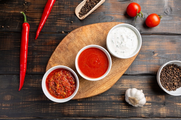 Photo different types of sauces in bowls on cutting board with garlic. on dark rustic