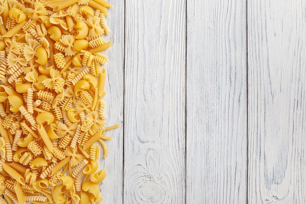 Different types and shapes of Italian pasta on white wooden background