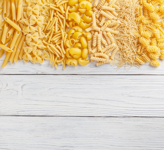 Different types and shapes of Italian pasta on white wooden background