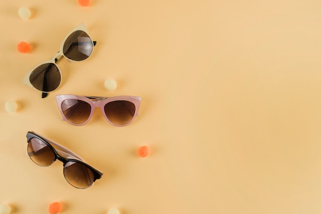 Photo different types of sunglasses with pom pom on beige backdrop