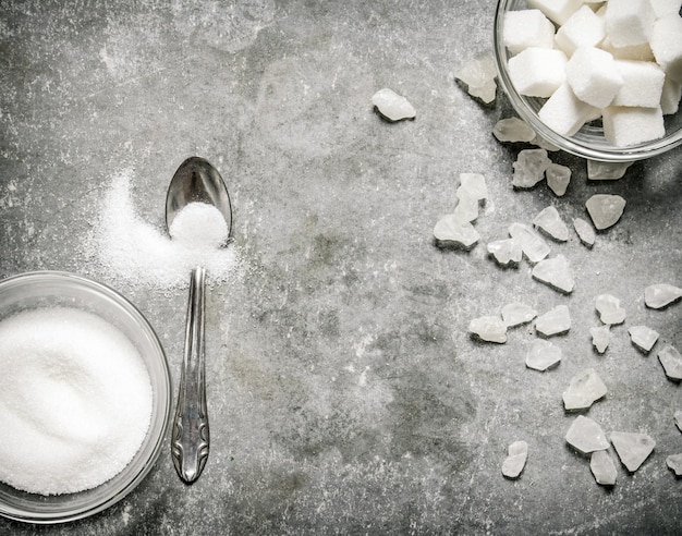 Different types of white sugar in a glass and spoon. On a stone table.