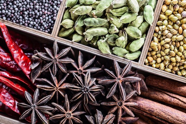 Different types of whole Indian spices in wooden box close-up top view.