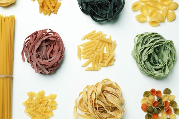 Different uncooked color pasta on white surface