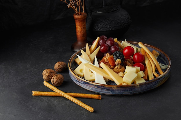 Different varieties of cheese and tomatoes on a large plate on a black background