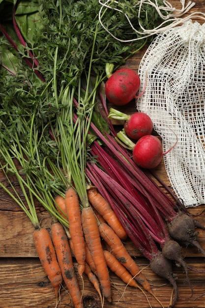 Different vegetables and net bag on wooden table flat lay