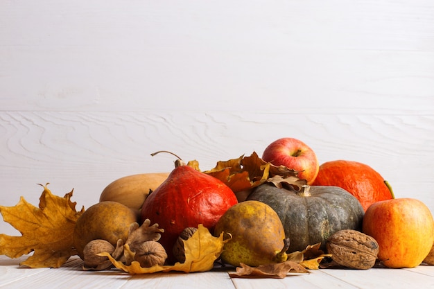 Different vegetables, pumpkins, apples, pears, nuts and dry yellow leaves on a white wooden background, copyspace. Harvest .