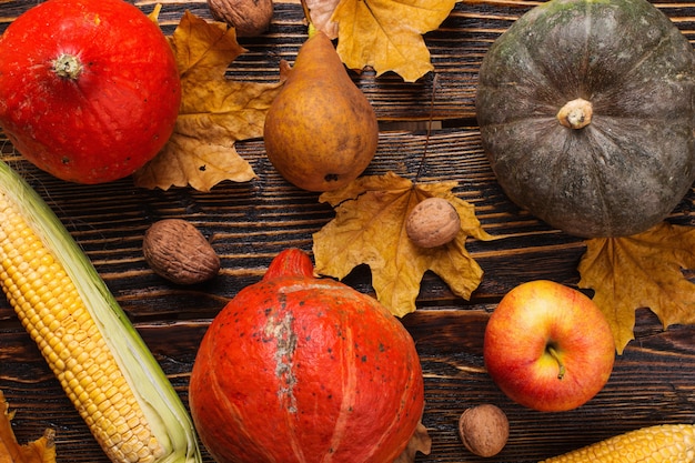 Different vegetables, pumpkins, apples, pears, nuts, tomatoes, corn, dry yellow leaves on wooden background. Autumn mood, flat lay. Harvest .