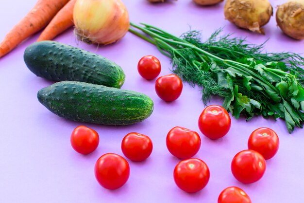 紫色の表面にあるさまざまな野菜、野菜-ジャガイモ、ニンジン、タマネギ、トマト、きゅうり、緑。健康的なダイエット。