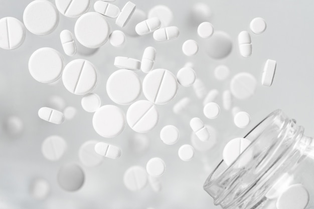 Различные белые медицинские таблетки, вылетающие из стеклянной банки