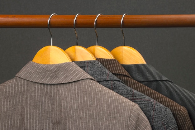На вешалке для хранения одежды вешаются разные женские офисные классические пиджаки. Выбор фасона модной одежды