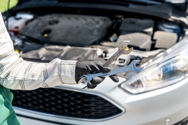 Different wrenches and spanners in hand over car engine