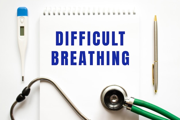 DIFFICULT BREATHING text written in a notebook lying on a desk and a stethoscope. Medical concept.