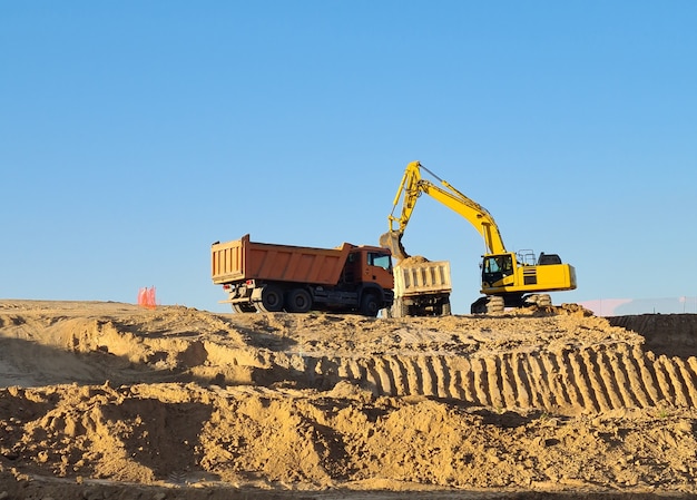 晴れた日に建設現場で2台のトラックを操作する掘削機。マドリードのバルデベバスで働く掘削機。
