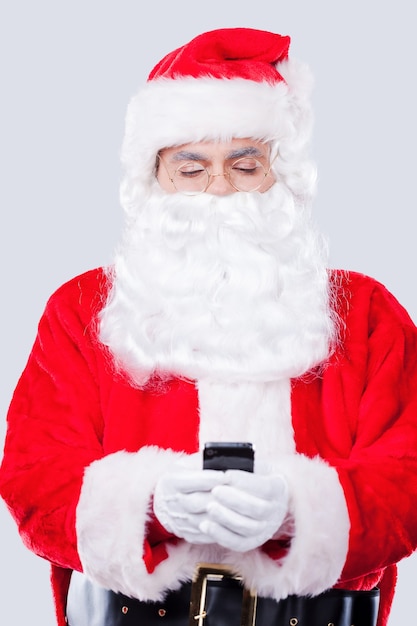 Digital age Santa. Traditional Santa Claus holding mobile phone while standing against grey background