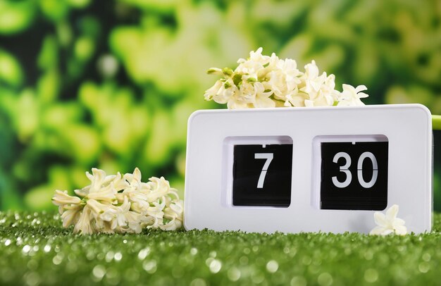 Digital alarm clock on green grass on nature background