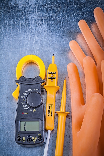 Digital ammeter electric tester electricians rubber gloves on metallic background electricity concept.