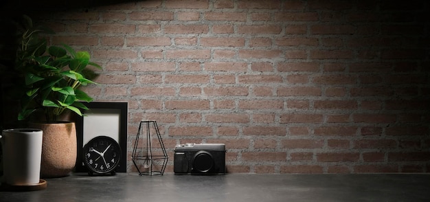 벽돌 벽 앞에 있는 흰색 테이블에 디지털 카메라 액자 알람 시계와 화분