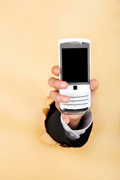 Digital composite image of hand holding mobile phone through beige background