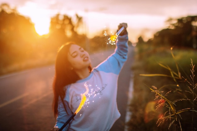 Photo digital composite image of woman holding firework on road during sunset