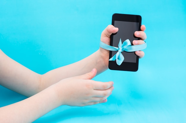 Digital detox concept. A children's hand with a smartphone is tied with a blue ribbon and a second hand reaches for them. Gadget addiction