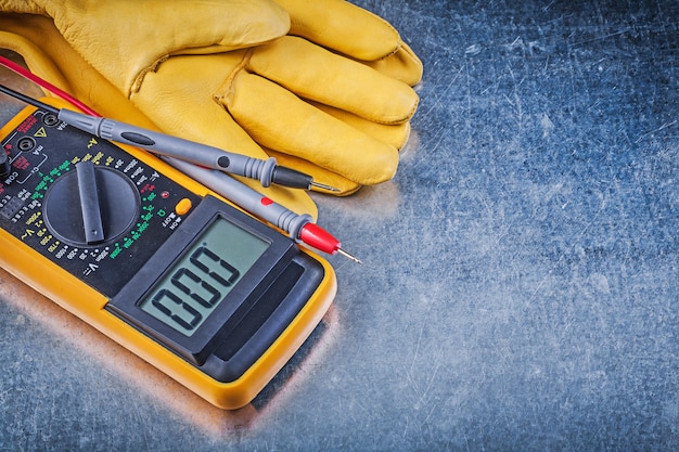 Digital electrical tester test leads pair of safety gloves on metallic background