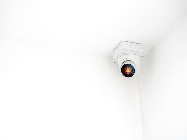 The digital eye technology on white security cctv camera or\
surveillance operating on ceiling in the corner room in the white\
wall building background with copy space