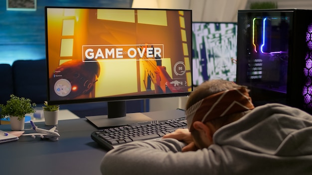 Digital gamer keeping his head on the office after losing first person shooter competition. Professional pro gamer playing online video games with new graphics on powerful computer from gaming room