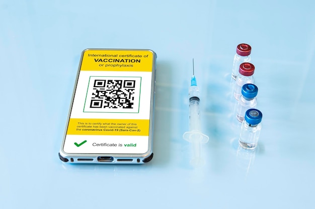 digital immunity passport with a covid-19 vaccination stamp and qr-code on a smartphone screen with vaccine, protective mask and syringe on a blue background. flat lay.