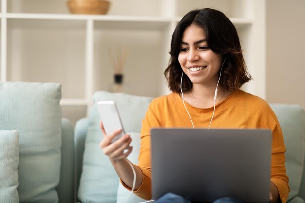 Foto tempo libero digitale sorridente donna mediorientale in appoggio con laptop e smartphone