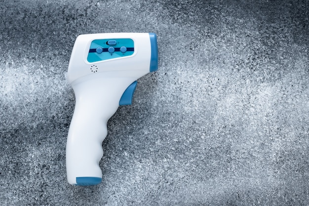 Digital medical infrared forehead thermometer gun non-contact of measuring temperature, for coronavirus (COVID-19) testing. Gray grunge concrete wall