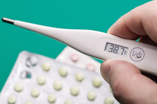 Digital medical thermometer with readings in the hand of man. Pain relief pills. Close-up. Health care concept.