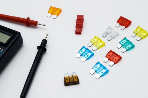 Digital multimeter for measuring electrical elements and car fuses on a white background