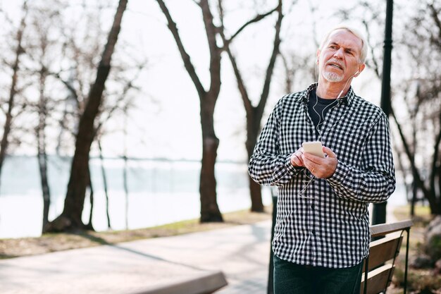 Digital music. Pleased senior man leaning on bench and listening to music