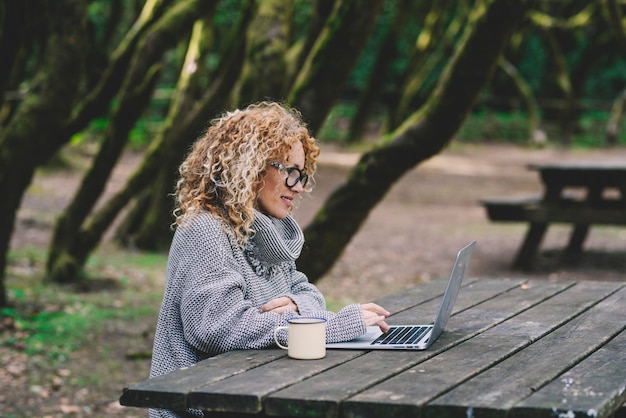 디지털 유목민 생활 방식 개념 젊은 여성은 나무 탁자 책상에서 노트북을 사용하고 무선 컴퓨터 연결을 통해 스마트 작업 활동에 바쁜 야외 사무실과 여성 사람들
