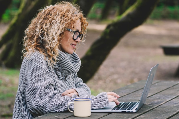 디지털 유목 생활 컨셉 젊은 여성은 나무 테이블 책상에 노트북을 사용 대안 야외 사무실과 무선 컴퓨터 연결과 함께 스마트 작업 활동에 몰두하는 여성 비즈니스