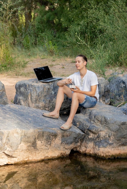 Digital nomad male taking advantage of his break to eat a picnic in nature next to a green river