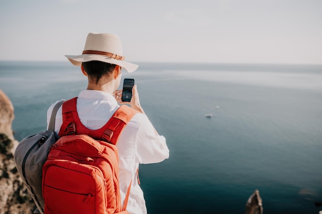 Digital nomad man in the hat a businessman with a laptop sits on the rocks by the sea during sunset