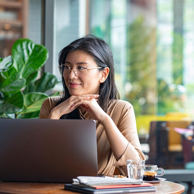 Digital Nomads Smiling Asian Businesswoman Sitting at a Cafe and Working on Her Laptop Computer