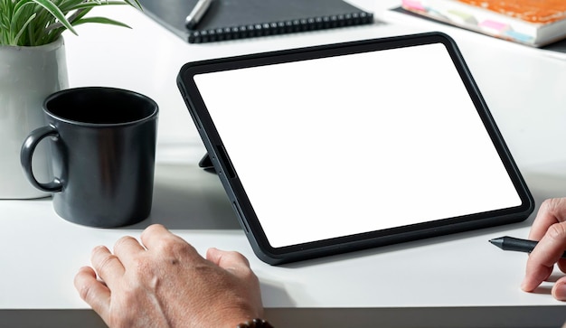 Digital portable tablet computer white screen mockup. Man working on digital tablet at his desk.