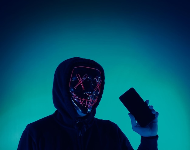 Concetto di sicurezza digitale hacker anonimo con maschera che tiene smartphone hackerato