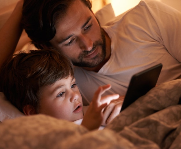 Digital story time A father and son lying in bed with an ereader