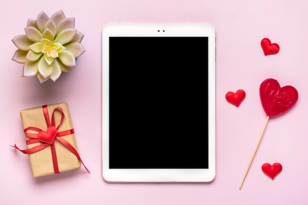 Digital tablet for chooses gifts makes purchase envelope red hearts on pink table