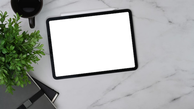 Цифровой планшет, кофейная чашка, комнатное растение и ноутбук на мраморном столе.