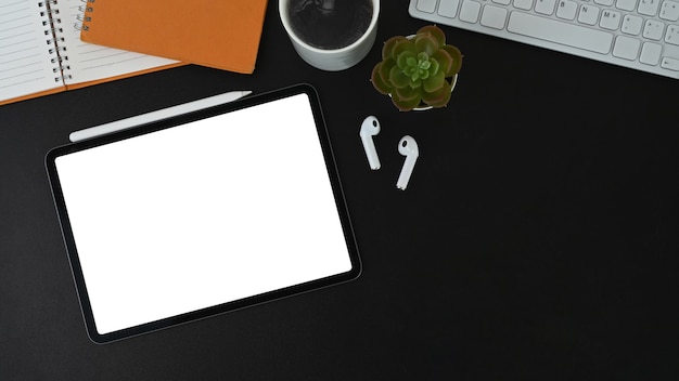 Digital tablet, coffee cup, keyboard and notebook on black leather.